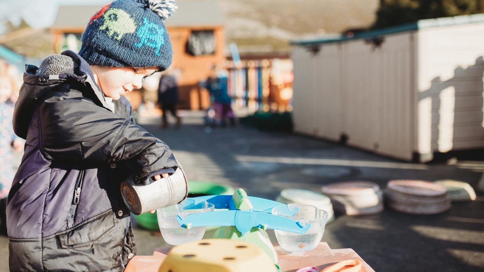 little boy pouring water in pre-school playground