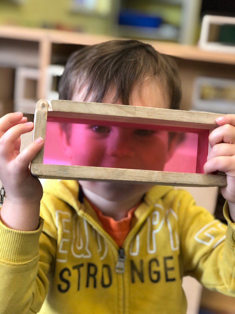 toddler looking through pink plastic window frame