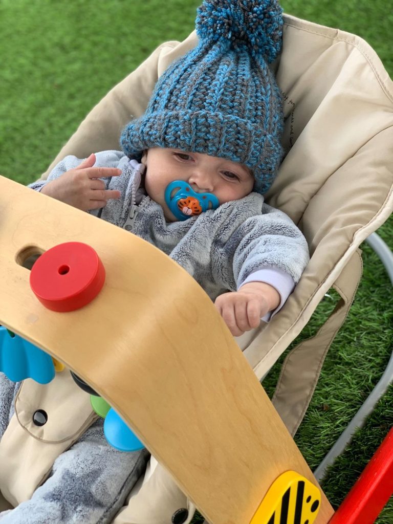 baby in bouncer wearing blue woolly hat