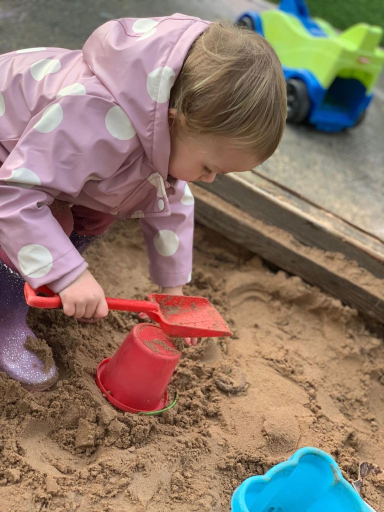 toddler wearing pink coat making sandcastles