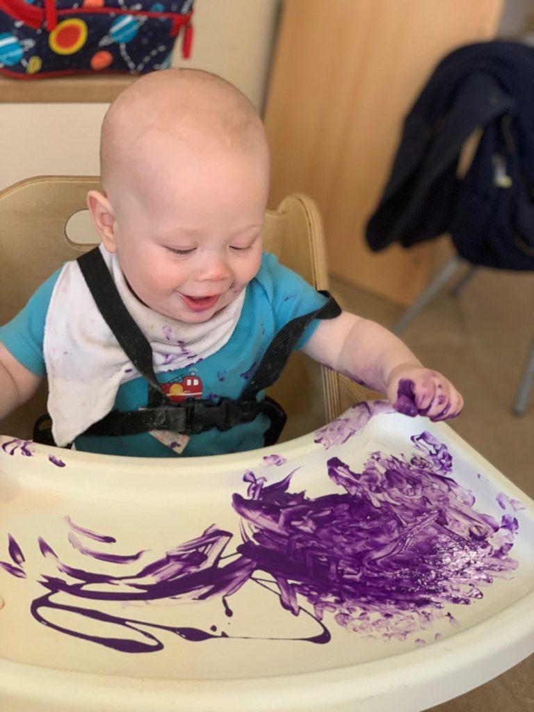 baby sitting at highchair playing with purple paint