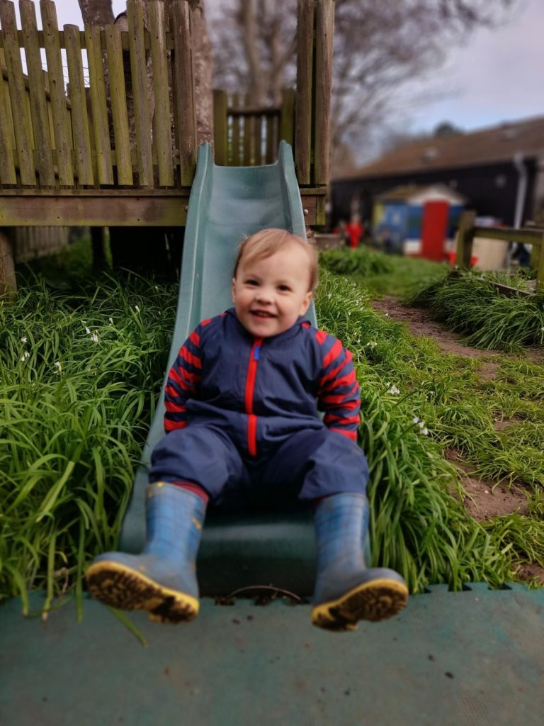 toddler sitting at the bottom of a slide, smiling