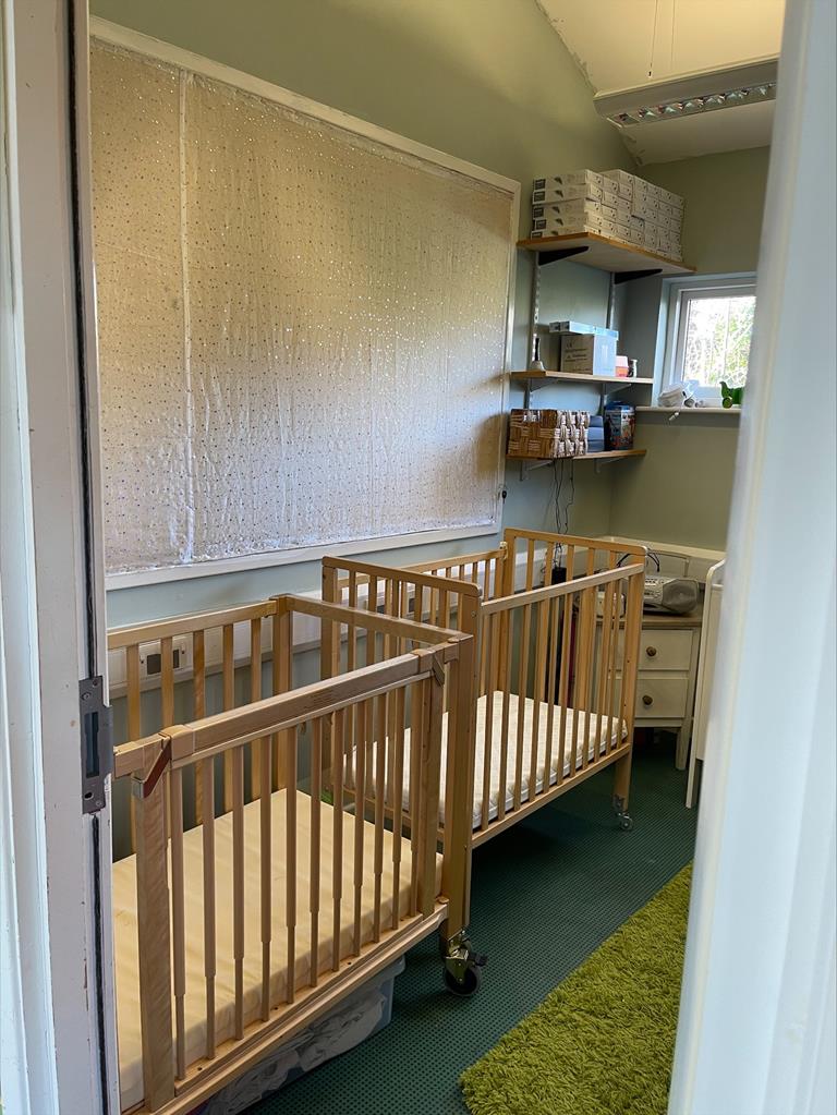 Nursery sleep room, with three wooden cots and a soft green rug on the floor.