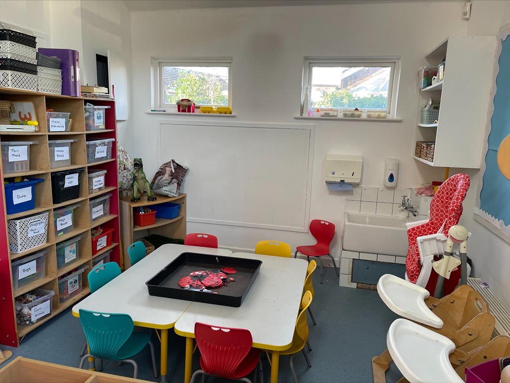 Nursery room, with low table seating for toddlers, toy storage, and wooden high chairs.